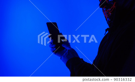 Anonymous hacker and face mask with smartphone in hand. Man in black hood shirt trying to hack personal data from mobile phone. Represent cyber crime data hacking or personal data stealing concept. 90316332