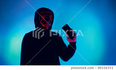 Anonymous hacker and face mask with smartphone in hand. Man in black hood shirt trying to hack personal data from mobile phone. Represent cyber crime data hacking or personal data stealing concept. 90316351