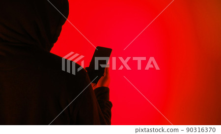 Anonymous hacker and face mask with smartphone in hand. Man in black hood shirt trying to hack personal data from mobile phone. Represent cyber crime data hacking or personal data stealing concept. 90316370