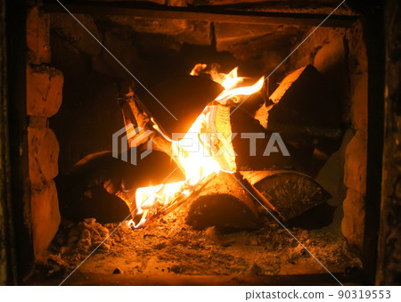 Warm light of a burning bright fire in a fireplace in old Russian stove. Flame and firewood background. Detail of interior. Warm light of a burning bright fire in a fireplace in old Russian stove. Flame and firewood background. Detail of interior. 90319553