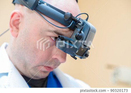 A male ophthalmologist checks a patient's vision with a binocular ophthalmoscope 90320173