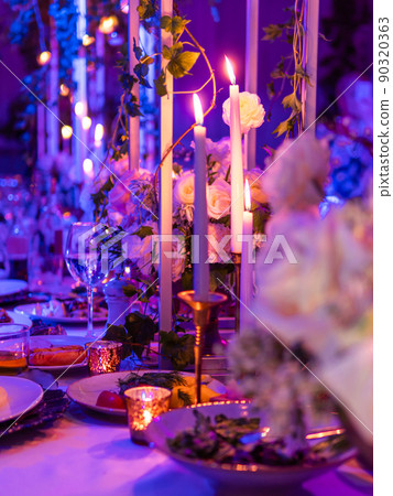 Table served for banquet with candles and floral compositions. Beautiful decorations in blue and purple electric light. Table served for banquet with candles and floral compositions. Beautiful decorations in blue and purple electric light. 90320363
