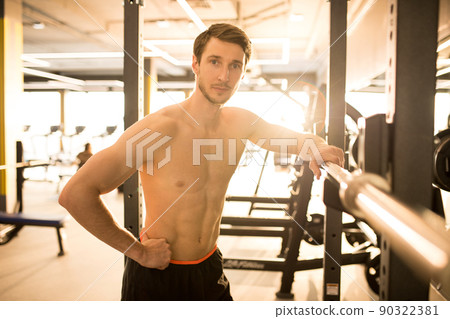 Handsome muscular man standing without t-shirt and looking at camera while training in sport gym Handsome muscular man standing without t-shirt and looking at camera while training in sport gym 90322381
