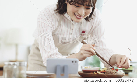 A young woman cooking while looking at her smartphone A young woman cooking while looking at her smartphone 90322478