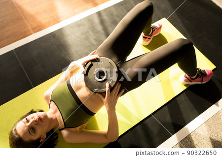 High view image of young sportswoman putting the weight on her stomach and training press on exercise mat 90322650
