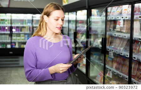 Positive woman chooses salami packaging in supermarket Positive woman chooses salami packaging in supermarket 90323972