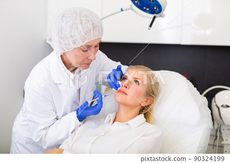 Cosmetologist doing botulotoxin injections for young woman Cosmetologist doing botulotoxin injections for young woman 90324199