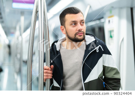 Young bearded man holding on handrails in subway car Young bearded man holding on handrails in subway car 90324404