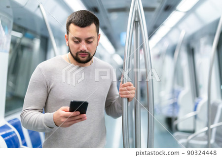 Portrait of european man standing in underground carriage and using phone 90324448