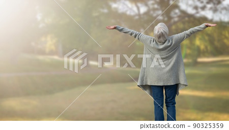 Rear view of caucasian senior woman with arms outstretched standing in park during foggy weather 90325359