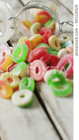 Vertical image of jelly candy spilling out of glass jar on wooden background Vertical image of jelly candy spilling out of glass jar on wooden background 90328926