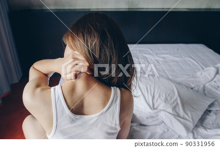 Back view of young Asian woman sitting on bed having neck pain and stretching her body after wake up in the morning. Back view of young Asian woman sitting on bed having neck pain and stretching her body after wake up in the morning. 90331956