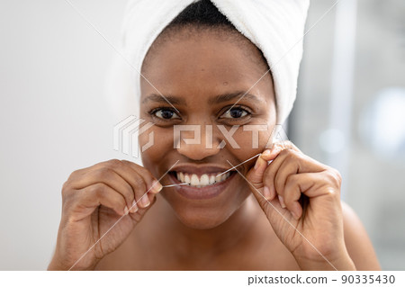 Portrait of african american mid adult woman using dental floss in bathroom 90335430
