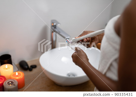Midsection of african american mid adult woman applying toothpaste on brush in bathroom 90335431