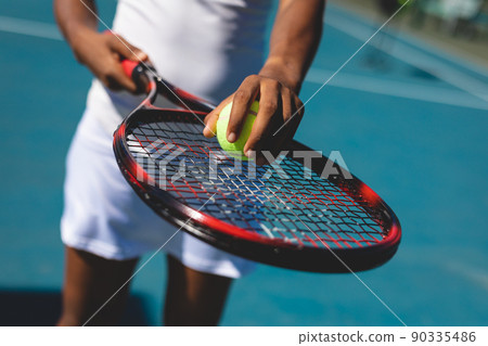 Midsection of african american female player holding ball on racket at tennis court on sunny day 90335486