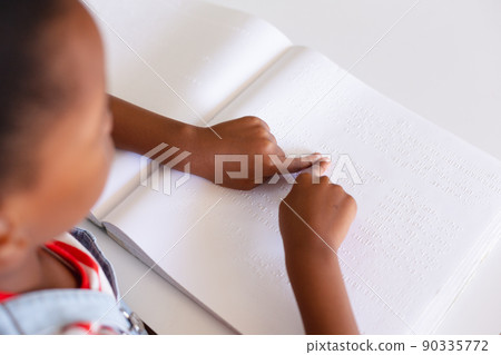 African american elementary schoolgirl touching braille book while studying at desk in class African american elementary schoolgirl touching braille book while studying at desk in class 90335772