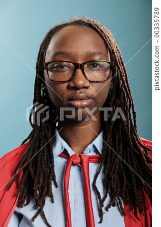 Portrait of brave superhero woman wearing mighty hero red cloak standing on blue background while looking at camera. Strong justice defender with superpower abilities posing for camera. 90335789
