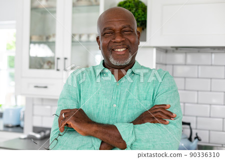 Portrait of smiling african american senior man with arms crossed standing in kitchen at home 90336310