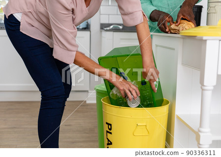 Midsection of senior woman dumping bottles in garbage can at home Midsection of senior woman dumping bottles in garbage can at home 90336311