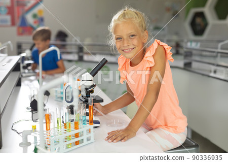 Portrait of smiling caucasian elementary schoolgirl sitting by microscope in school laboratory Portrait of smiling caucasian elementary schoolgirl sitting by microscope in school laboratory 90336935