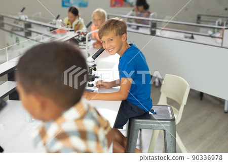 Smiling caucasian elementary boy looking at biracial male classmate in laboratory Smiling caucasian elementary boy looking at biracial male classmate in laboratory 90336978