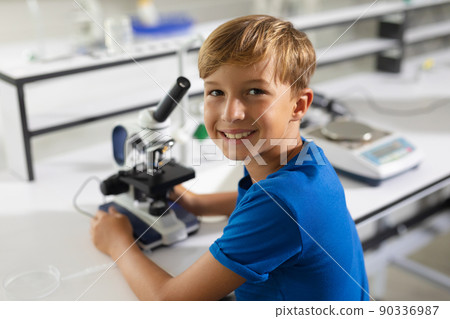 Portrait of smiling caucasian elementary schoolboy with microscope sitting at desk in laboratory Portrait of smiling caucasian elementary schoolboy with microscope sitting at desk in laboratory 90336987