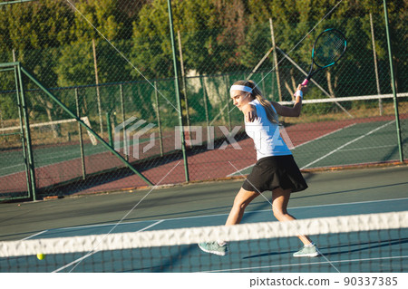 Full length of young female caucasian tennis player hitting ball at court on sunny day 90337385