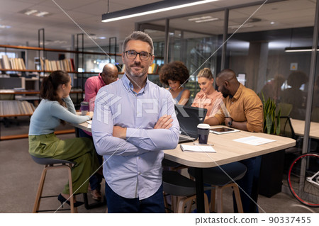 Portrait of mature caucasian businessman standing with arms crossed against biracial colleagues Portrait of mature caucasian businessman standing with arms crossed against biracial colleagues 90337455