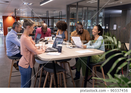 Multiracial male and female professionals working while using technologies and discussing at table Multiracial male and female professionals working while using technologies and discussing at table 90337456