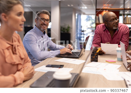 Portrait of smiling caucasian businessman sitting amidst colleagues during meeting at workplace Portrait of smiling caucasian businessman sitting amidst colleagues during meeting at workplace 90337467