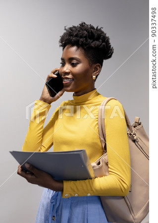 Smiling young african american businesswoman talking on smartphone against gray background Smiling young african american businesswoman talking on smartphone against gray background 90337498