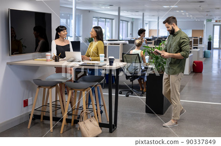 Caucasian businessman walking towards biracial businesswomen discussing during meeting in workplace Caucasian businessman walking towards biracial businesswomen discussing during meeting in workplace 90337849