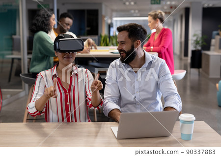 Happy caucasian businessman looking biracial businesswoman gesturing while experiencing vr headset Happy caucasian businessman looking biracial businesswoman gesturing while experiencing vr headset 90337883