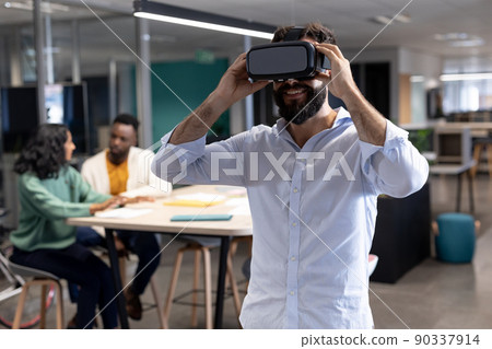 Smiling caucasian businessman wearing virtual reality simulator at modern workplace Smiling caucasian businessman wearing virtual reality simulator at modern workplace 90337914