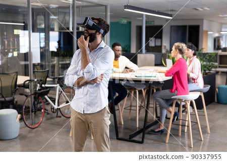 Thoughtful caucasian businessman wearing virtual reality simulator against biracial colleagues Thoughtful caucasian businessman wearing virtual reality simulator against biracial colleagues 90337955