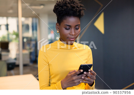 Young african american businesswoman text messaging through smartphone at workplace Young african american businesswoman text messaging through smartphone at workplace 90337956