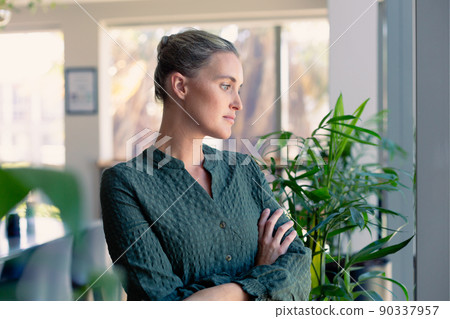 Caucasian businesswoman with arms crossed contemplating while looking away at workplace Caucasian businesswoman with arms crossed contemplating while looking away at workplace 90337957