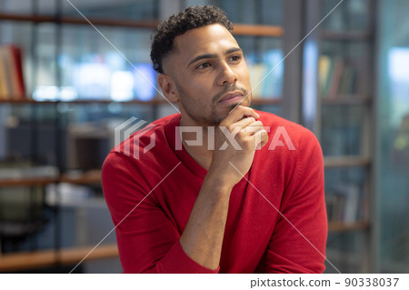 Thoughtful hispanic businessman with hand on chin while looking away at modern workplace 90338037