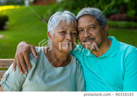 Close-up portrait of loving senior man with hand on wife's shoulder sitting on bench in park Close-up portrait of loving senior man with hand on wife's shoulder sitting on bench in park 90338185