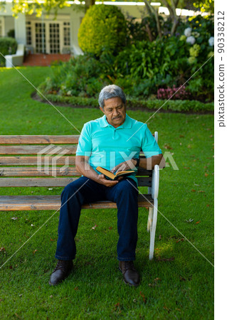 Full length of biracial senior man reading book while sitting on bench against plants in park Full length of biracial senior man reading book while sitting on bench against plants in park 90338212