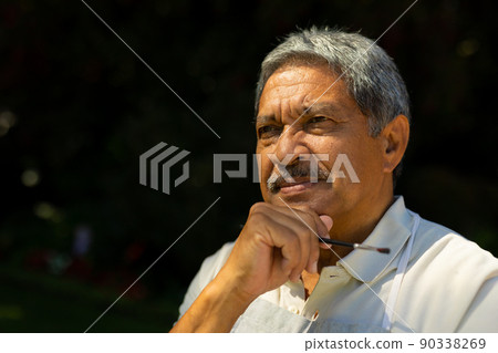 Close-up of thoughtful biracial senior man holding paintbrush with hand on chin looking away in yard Close-up of thoughtful biracial senior man holding paintbrush with hand on chin looking away in yard 90338269