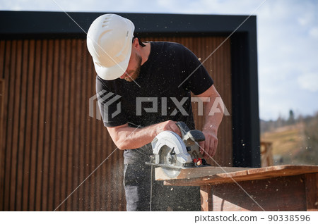 Carpenter using circular saw for cutting wooden plank. Man worker building wooden frame house. Carpentry concept. Carpenter using circular saw for cutting wooden plank. Man worker building wooden frame house. Carpentry concept. 90338596
