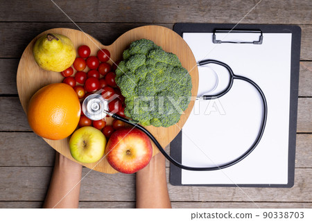 African american woman holding heart shape with vegetables, fruits, stethoscope by report on table 90338703