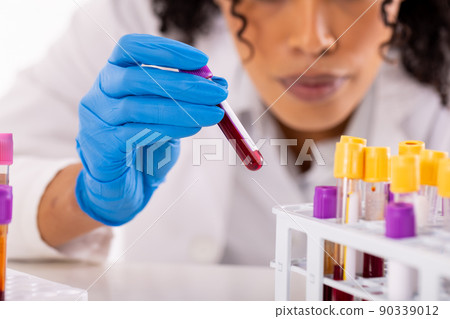 Midsection of african american mid adult female doctor placing test tubes in tray on table 90339012