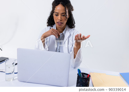 African american mid adult female doctor gesturing while video conferencing over laptop, copy space African american mid adult female doctor gesturing while video conferencing over laptop, copy space 90339014