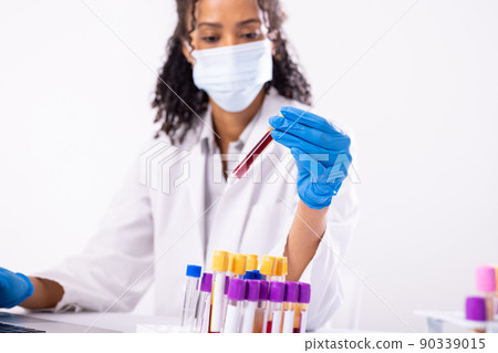 African american mid adult female doctor wearing mask holding test tubes against white background African american mid adult female doctor wearing mask holding test tubes against white background 90339015