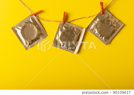 Close-up of condom packages hanging on clothesline with clothespins against yellow background 90339017