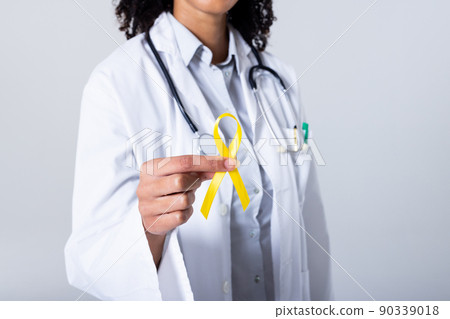 Midsection of african american mid adult female doctor holding yellow sarcoma awareness ribbon Midsection of african american mid adult female doctor holding yellow sarcoma awareness ribbon 90339018