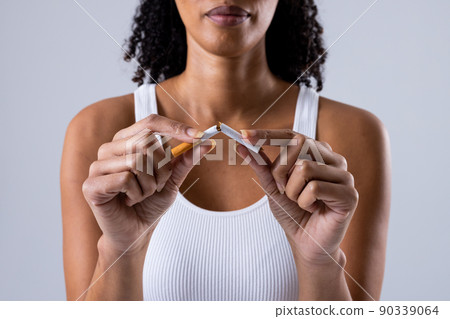 Midsection of african american mid adult woman breaking cigarette against white background Midsection of african american mid adult woman breaking cigarette against white background 90339064