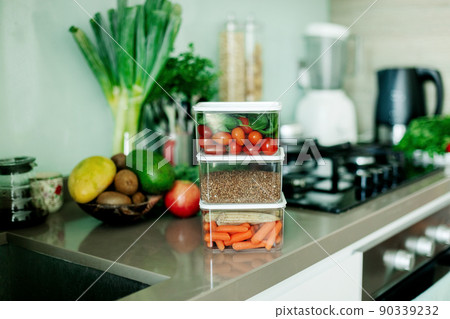 Fresh various vegetables and buckwheat in a container are on the table in the kitchen, the food is ready to eat. 90339232